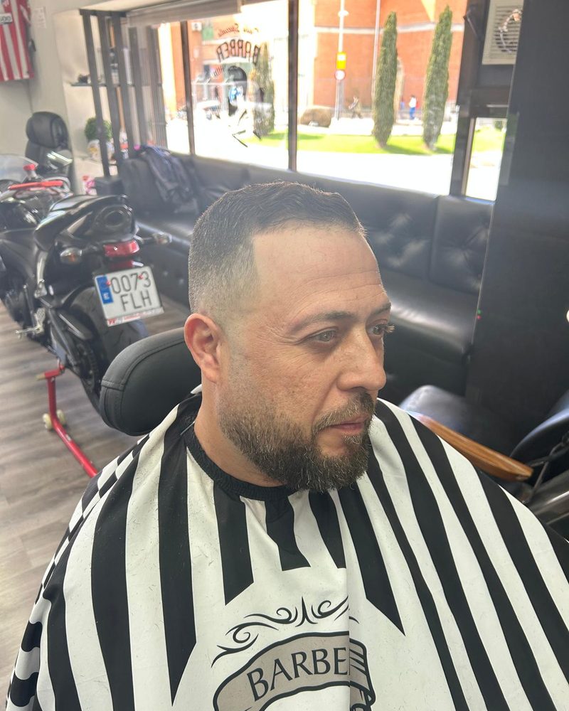 Corte con degradado y la barba arreglada, de perfil.