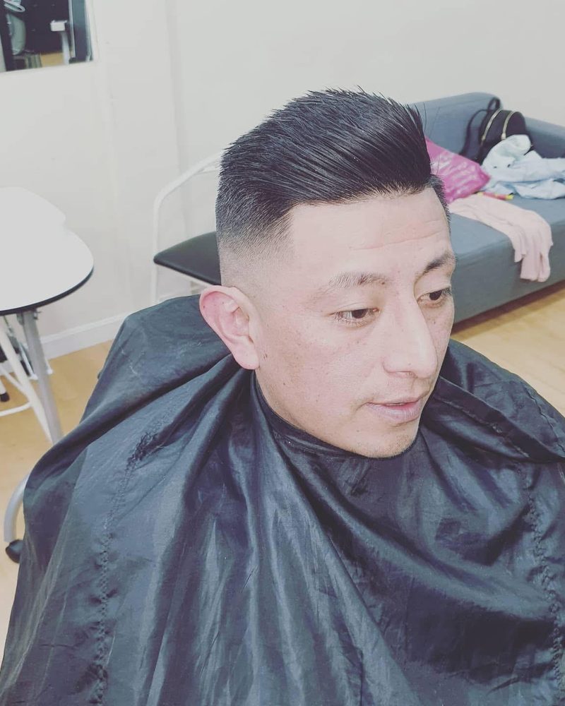 Corte con degradado y el pelo peinado hacia atrás.