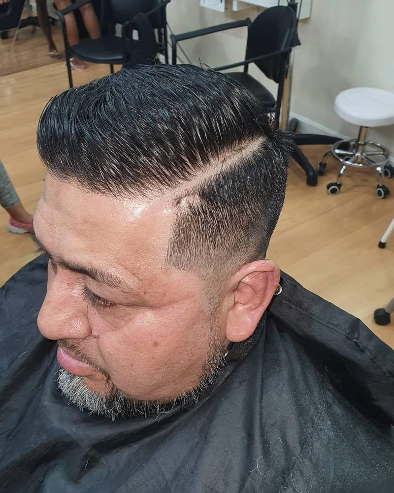 Corte con raya y degradado, el pelo peinado hacia atrás.