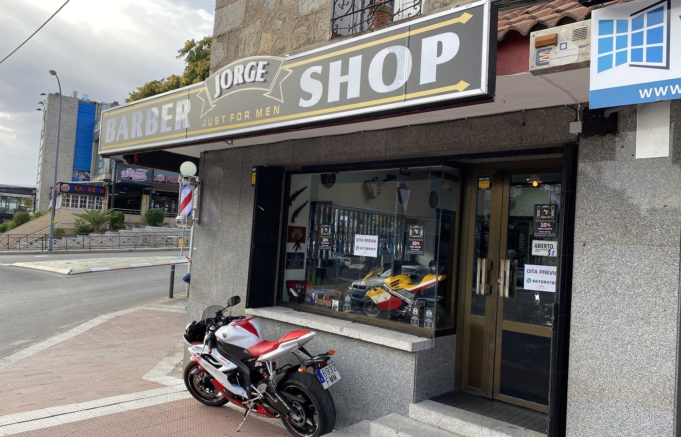 La fachada de Jorge Barber Shop desde la calle, con el rótulo a todo lo ancho y una moto deportiva aparcada delante.